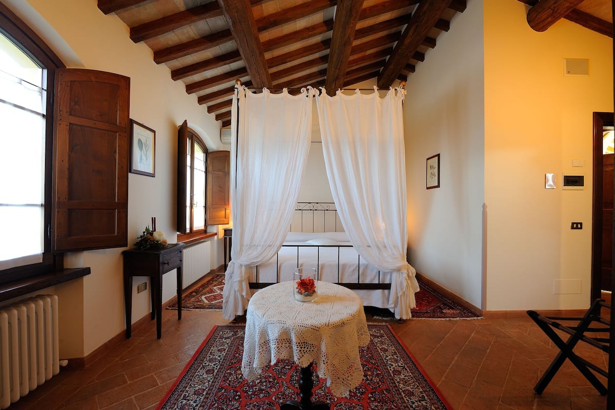 A bedroom with a bed, a small round table with a vase, and a window with curtains.