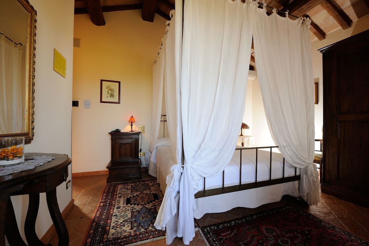 A bedroom with a four-poster bed, a nightstand with a lamp, a wooden dresser, and a patterned rug.