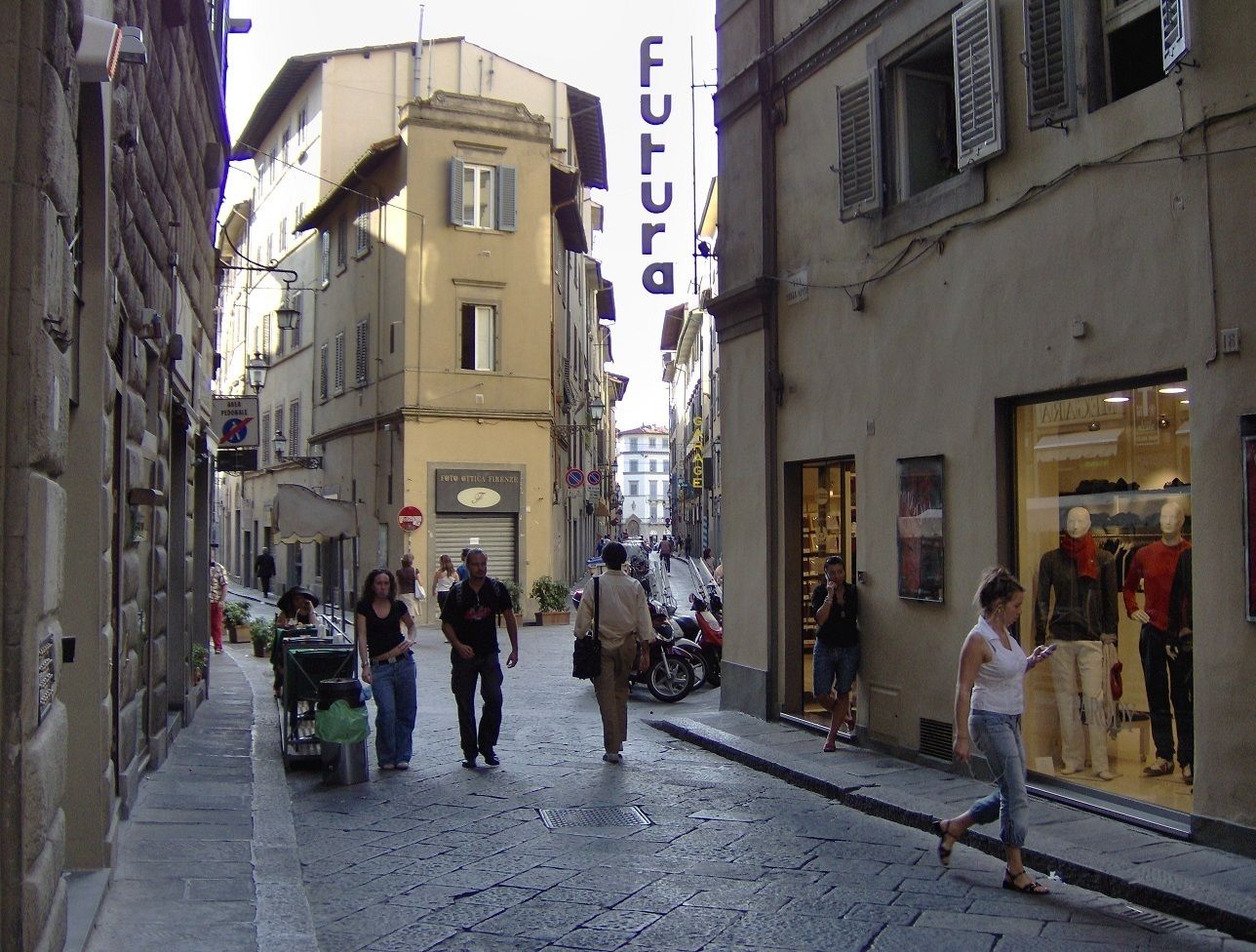 A narrow street with pedestrians, a shop with mannequins, and a building with a 'Futura' sign.