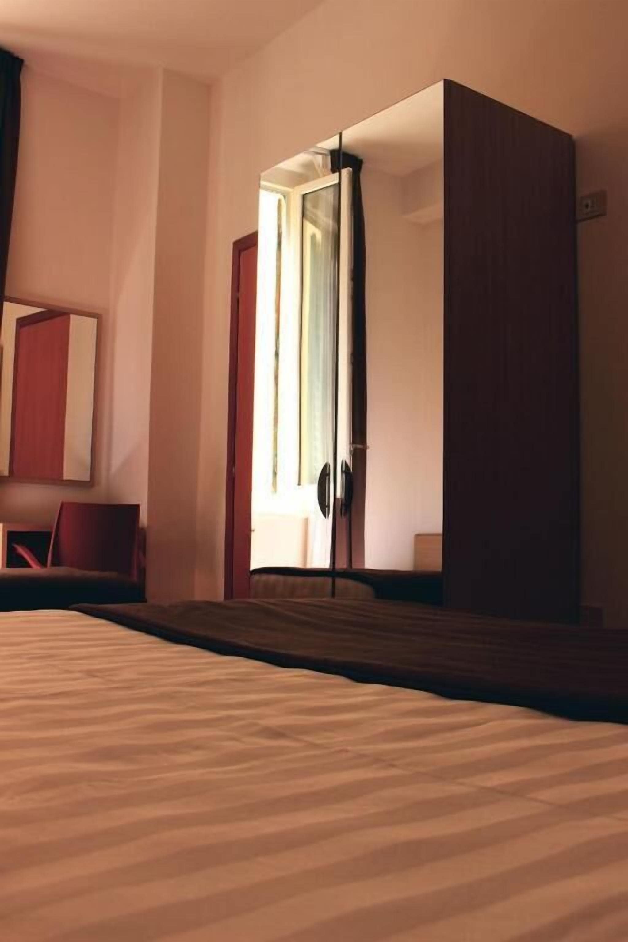 A hotel room with a bed, a wardrobe, a mirror, and a window with curtains.