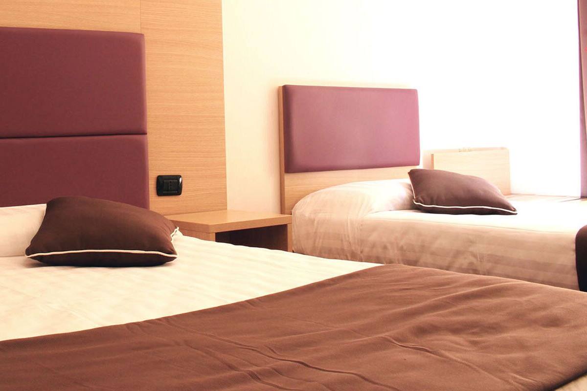Quarto de hotel com duas camas, cada uma com cabeceira e almofadas.