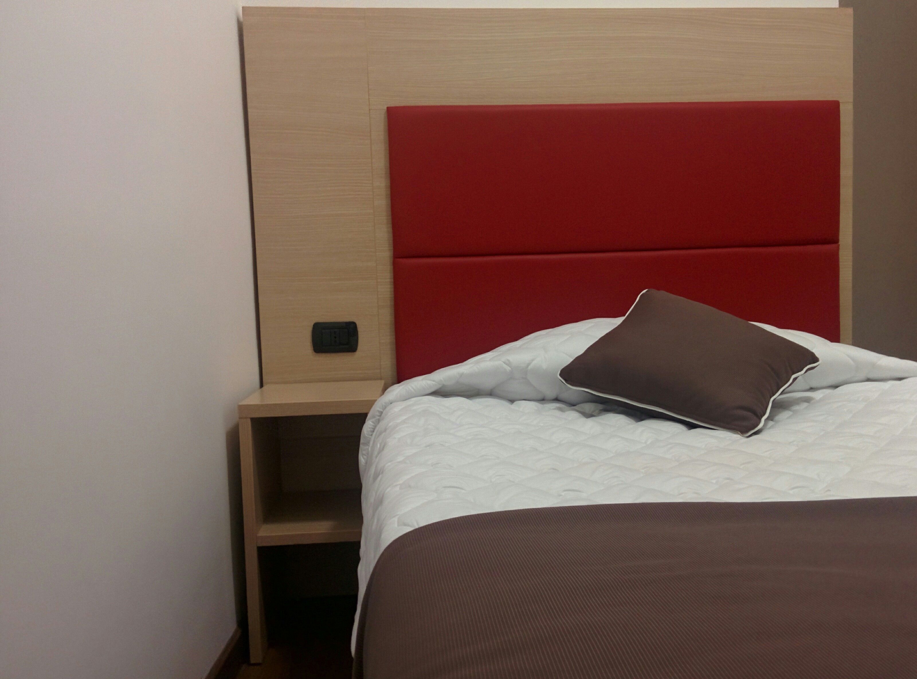 Ein Bett mit rotem Kopfteil, einem braunen Kissen und einer weißen Tagesdecke.