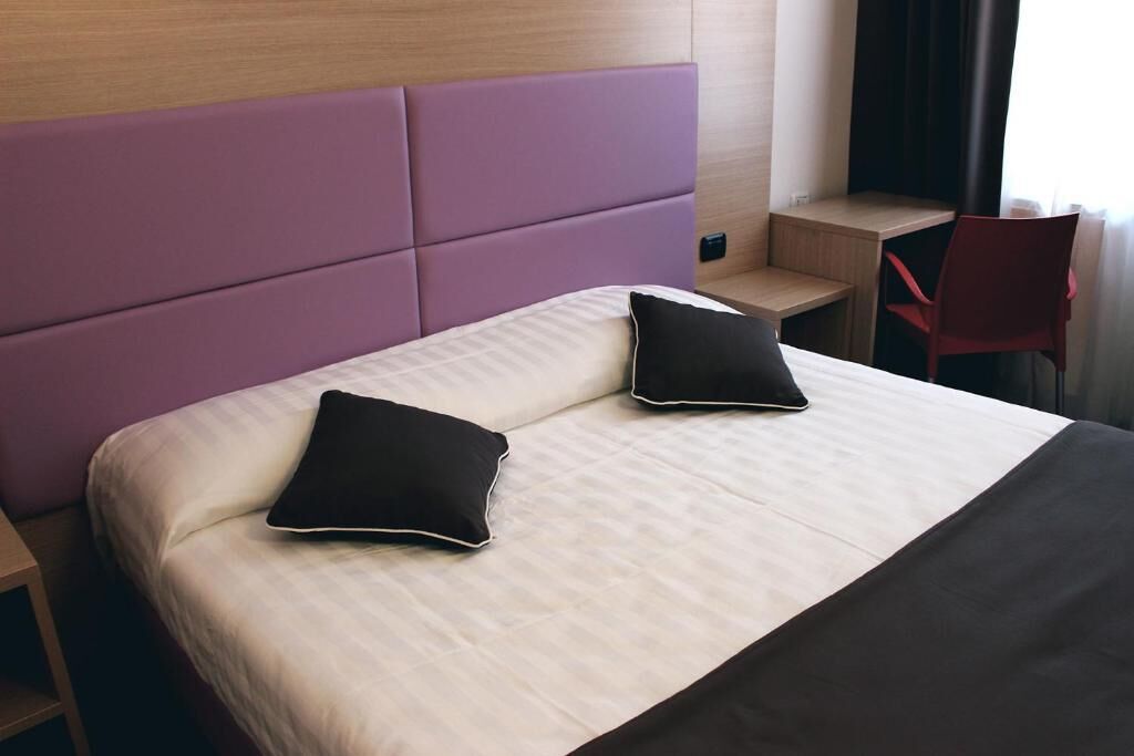 Habitación de hotel con una cama grande, dos almohadas, una mesita de noche pequeña, una silla y un escritorio.