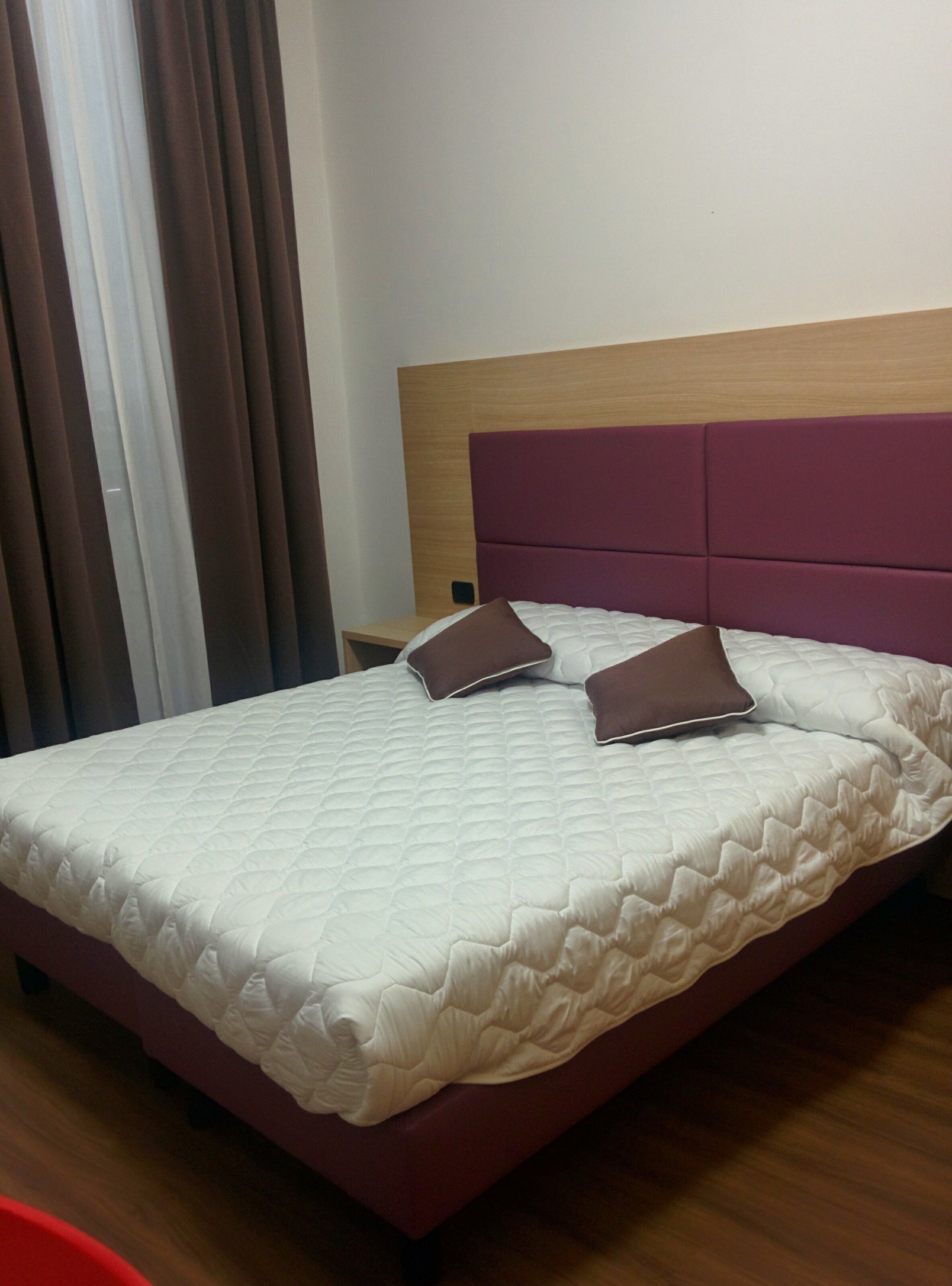Una habitación de hotel con una cama, cabecero de madera y una ventana con cortinas.