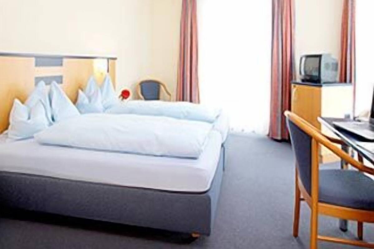 A hotel room with a bed, a desk, a chair, a television, and curtains.
