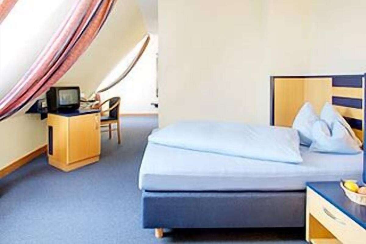 A bedroom with a bed, a desk, a chair, and a television.