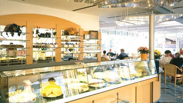 Eine Bäckereitheke mit einer Glasvitrine, Regale voller Backwaren und eine Sitzgelegenheit mit Stühlen.