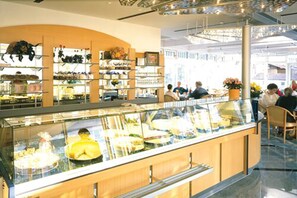 Un comptoir de boulangerie avec une vitrine réfrigérée, des étagères remplies de produits de boulangerie et un espace avec des chaises où les clients peuvent s’asseoir.