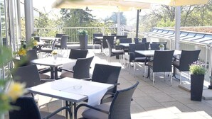 Ein Terrassenbereich im Freien mit Tischen und Stühlen, einige mit Sonnenschirmen.