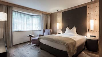 Et moderne hotelværelse med en stor seng, et lille rundt bord, en stol og et stort vindue med gardiner.
