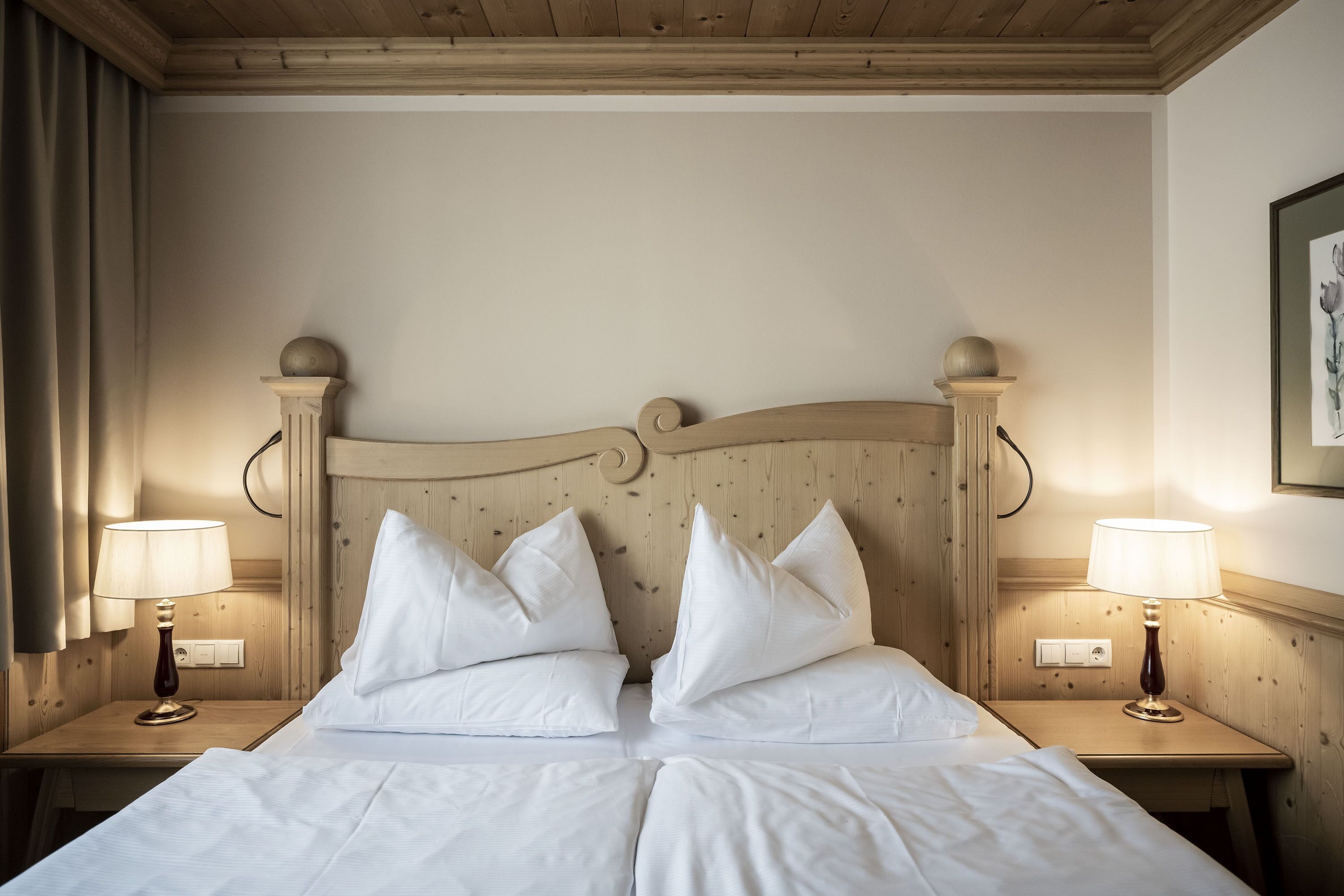 Un lit double avec du linge de lit blanc, deux lampes de chevet et une tête de lit en bois.