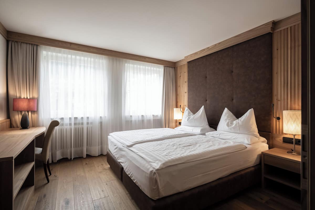 A hotel room with a large bed, a desk, and a chair.