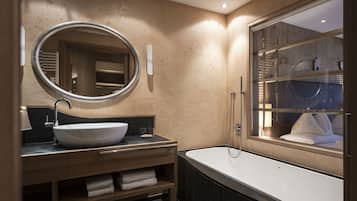 Un baño moderno con un espejo ovalado grande, un lavamanos independiente, una bañera y una ventana con vistas a la habitación.