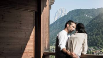 A couple standing on a balcony overlooking a mountainous landscape with a prominent peak in the background.