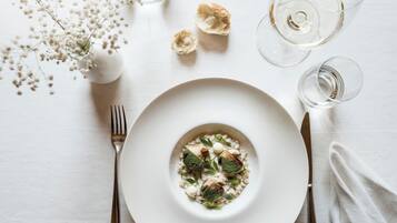 A white plate with a dish of food, a fork, a knife, and two wine glasses on a white table.