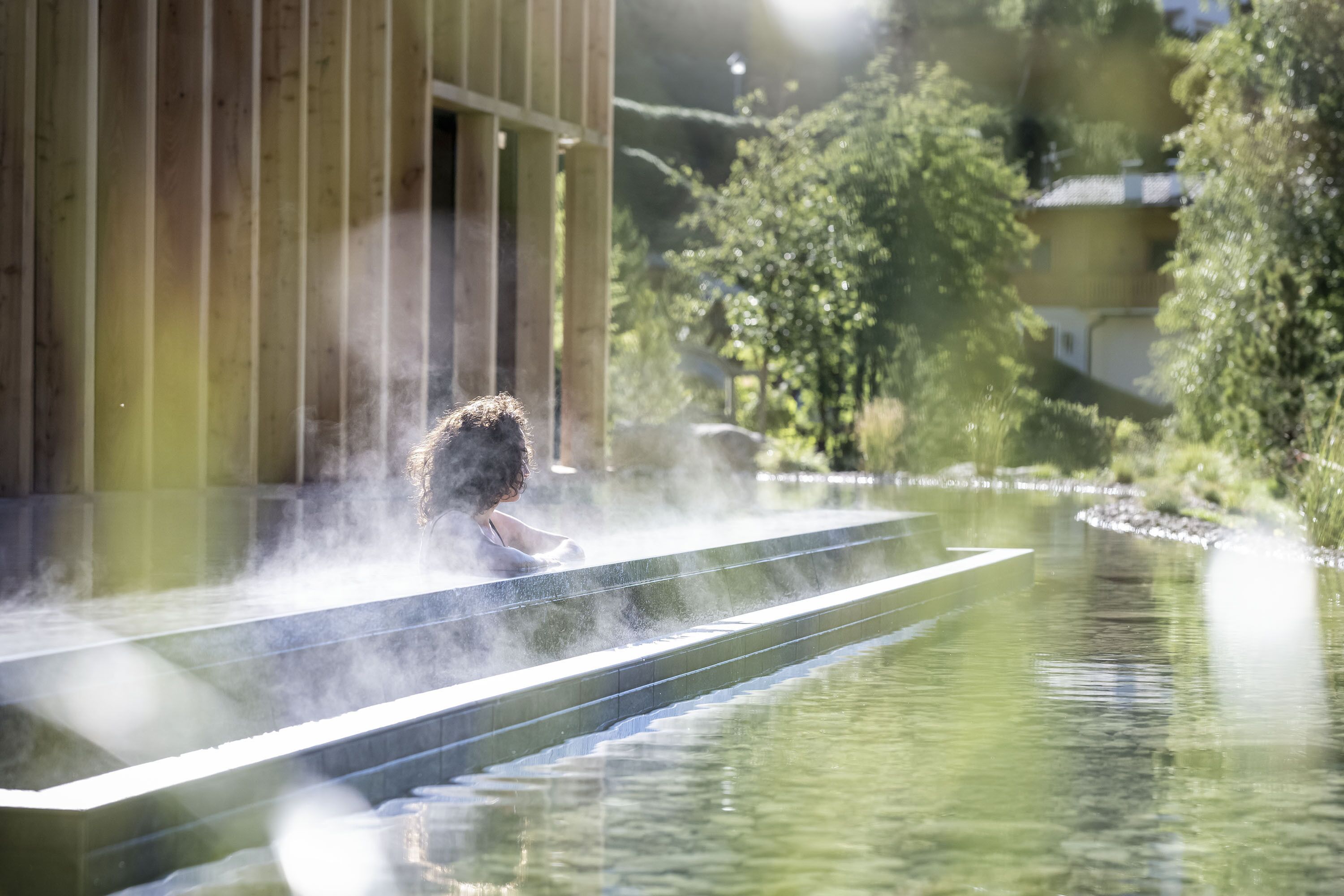 A person relaxing in a hot spring with a wooden structure in the background.