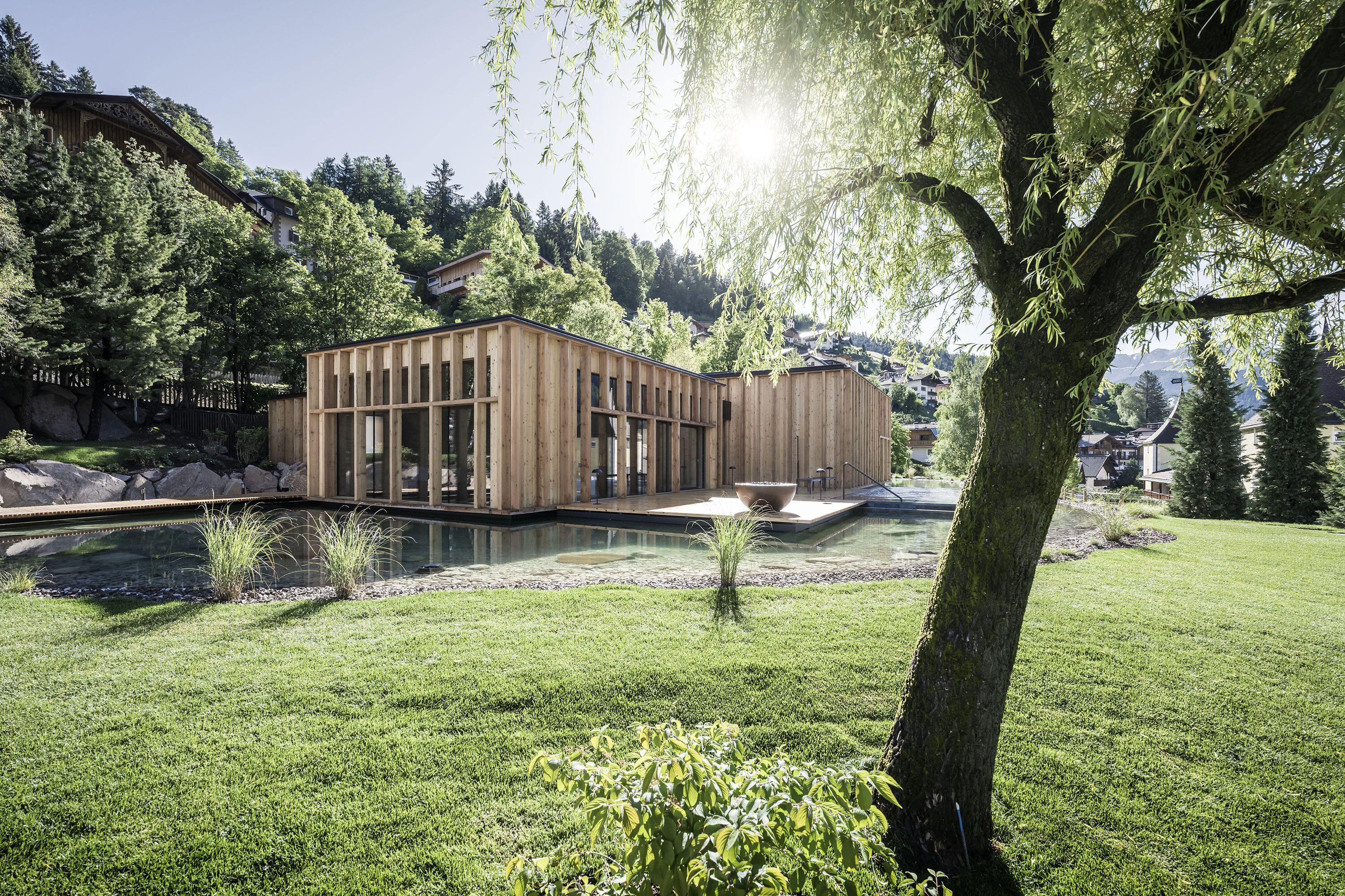 A modern building with a wooden facade, surrounded by a well-maintained lawn and a small pond.