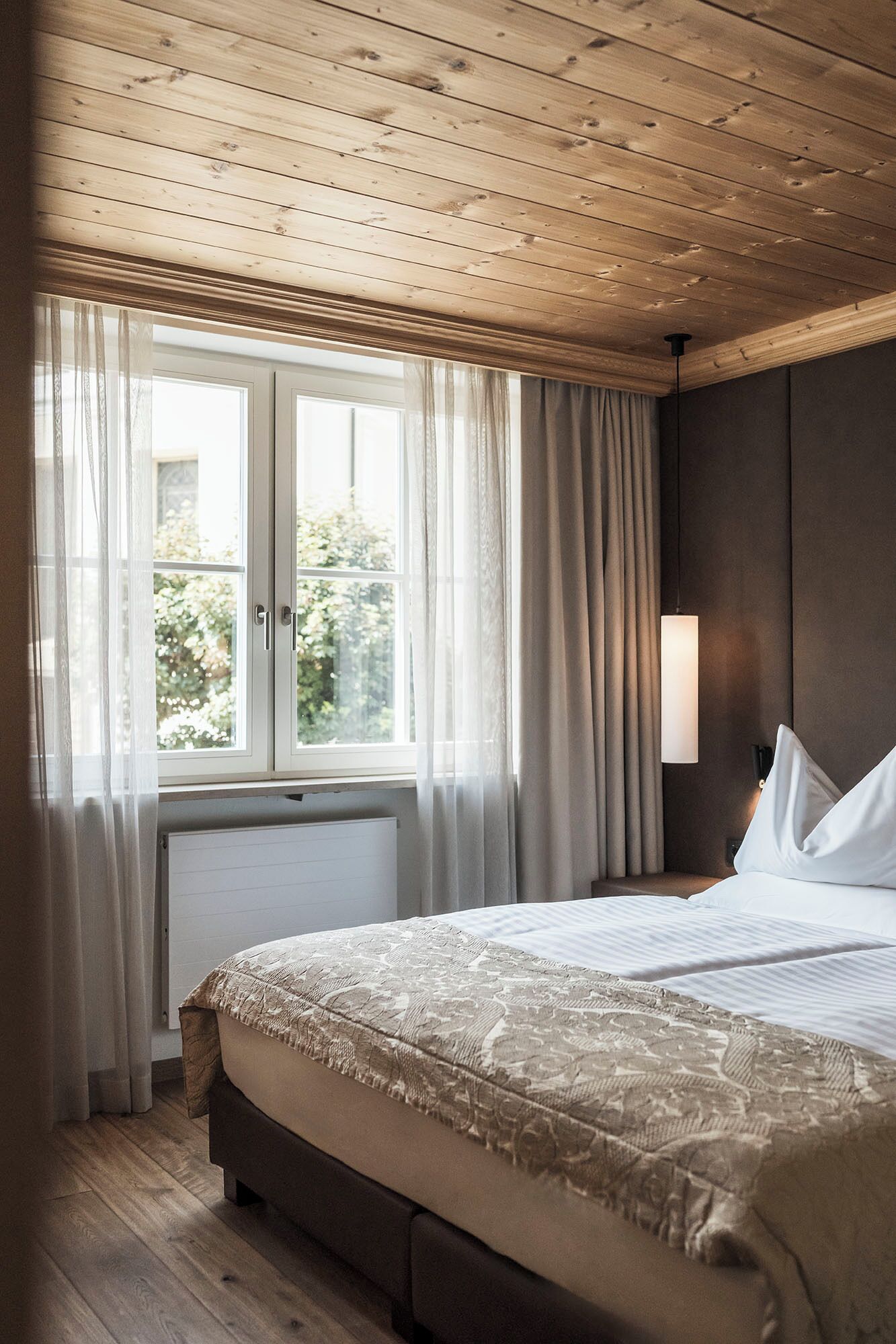 A bedroom with a large bed, wooden ceiling, and a window with curtains.