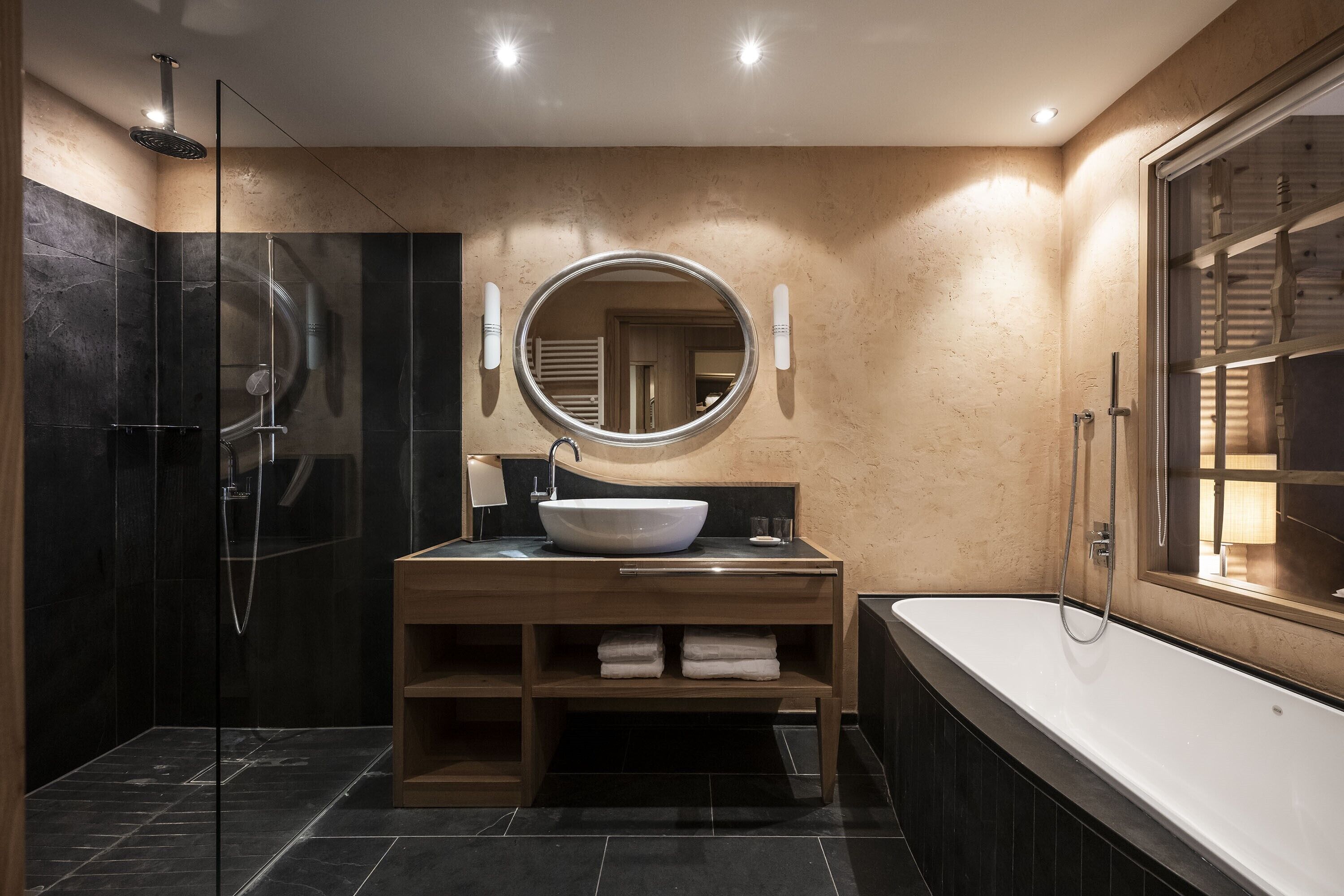 A modern bathroom with a glass-enclosed shower, a wooden vanity with a large mirror, and a freestanding bathtub.