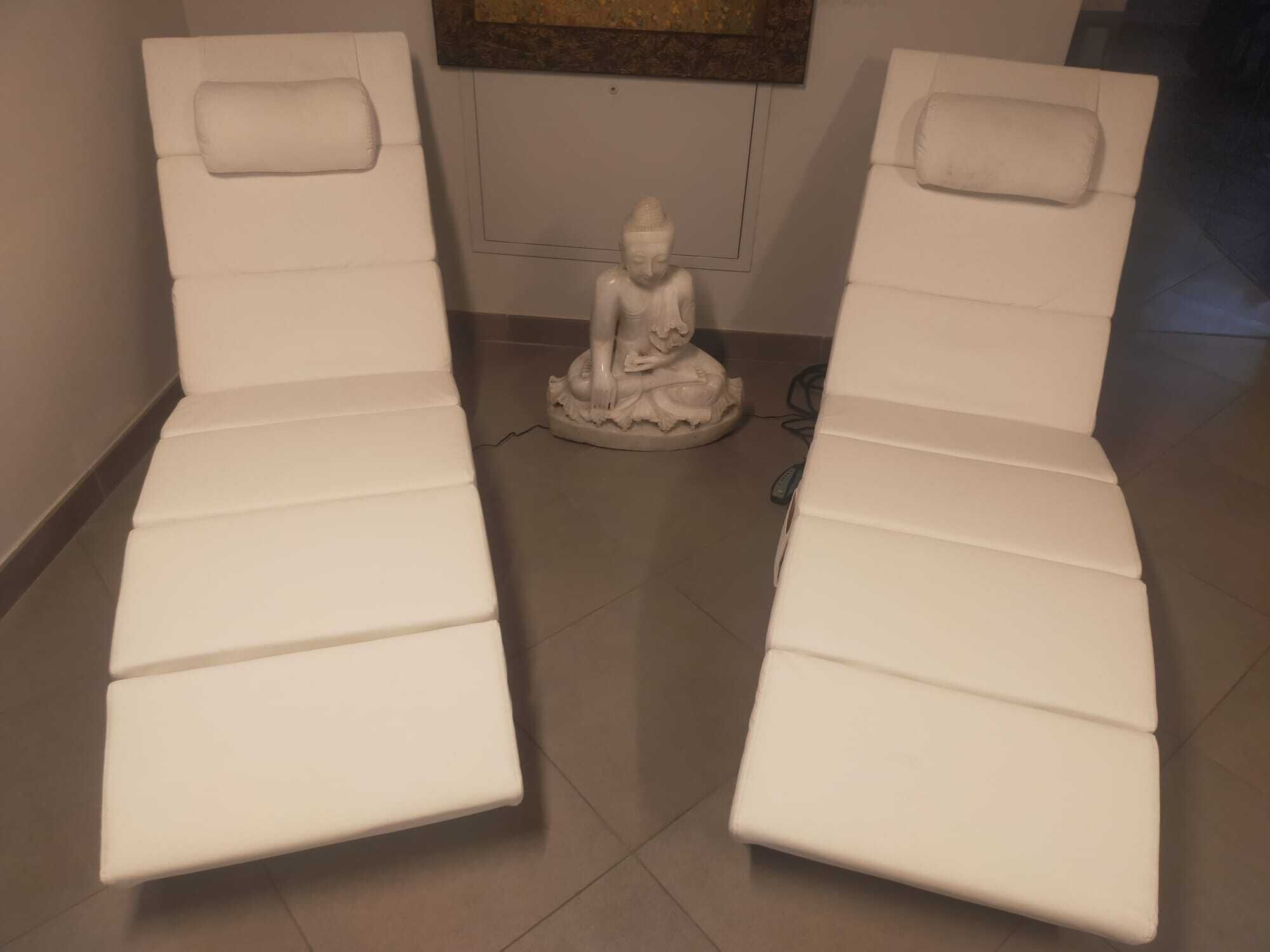 Dos sillas de masaje blancas con una pequeña estatua de una figura sentada en el medio.