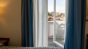 A room with a bed, a window with curtains, and a view of buildings outside. - Maritan Hotel & Spa (Padova)