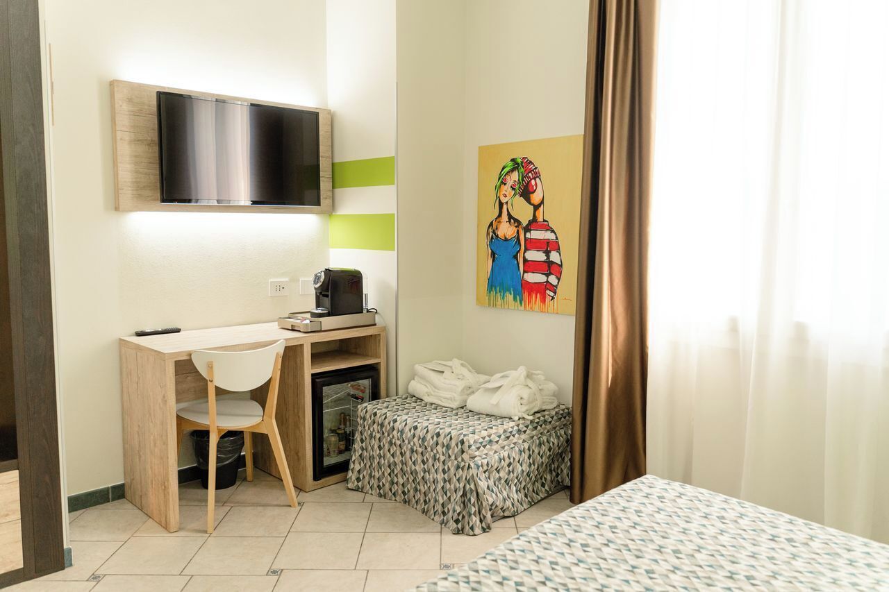 Een compacte hotelkamer met een houten bureau, een aan de muur bevestigde televisie, een kleine koelkast en een bed met beddengoed met een patroon.