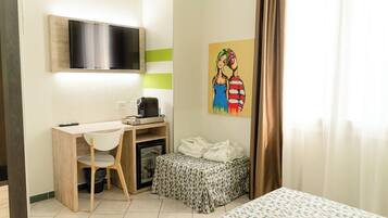 Een compacte hotelkamer met een houten bureau, een aan de muur bevestigde televisie, een kleine koelkast en een bed met beddengoed met een patroon.