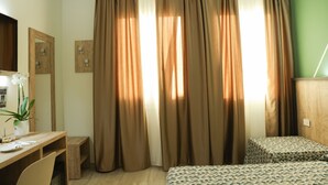 A room with a wooden desk, two beds with patterned bedding, a potted plant, and curtains. - Maritan Hotel & Spa (Padova)