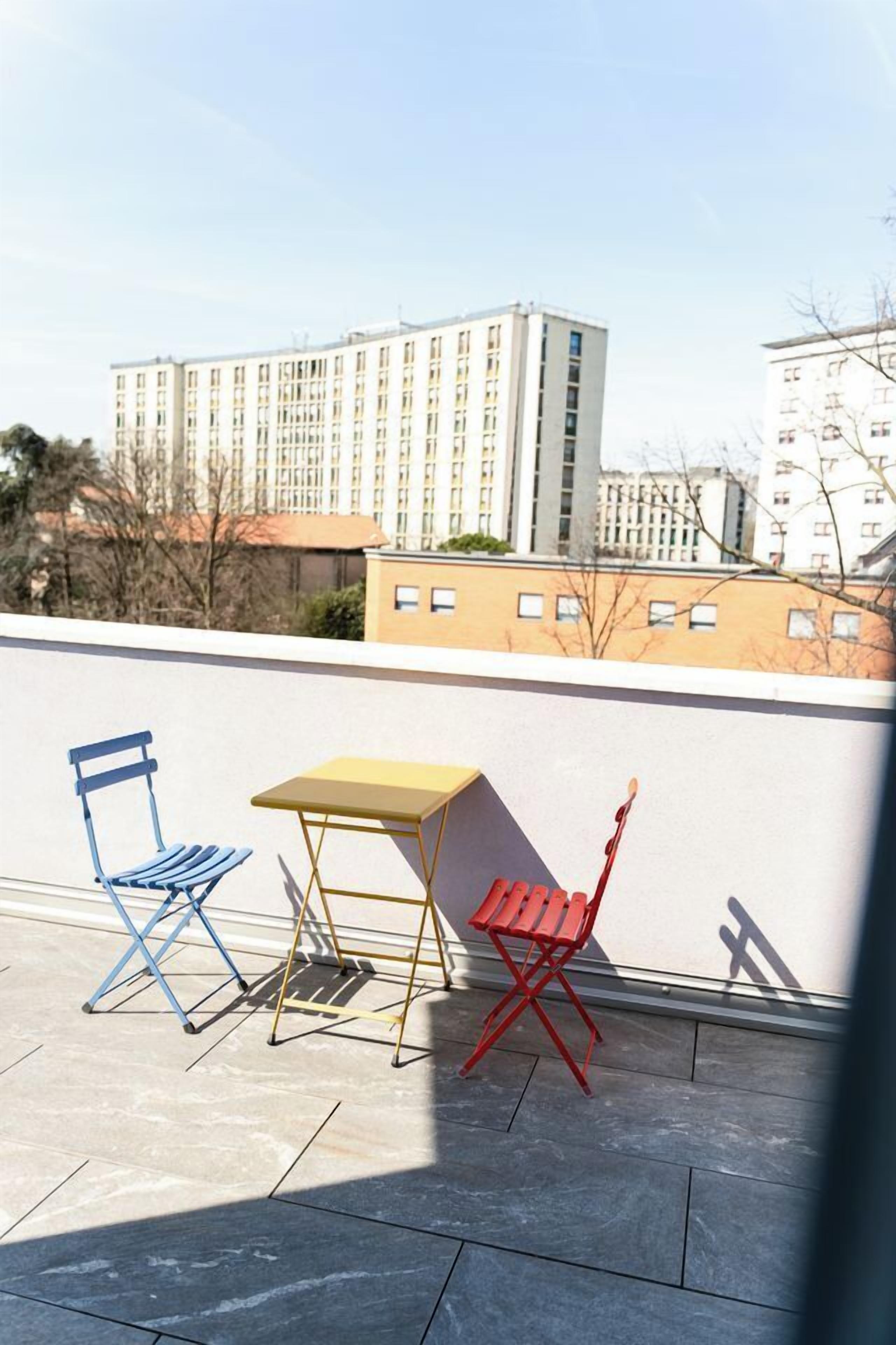 Een terras op het dak met twee stoelen en een kleine tafel, met uitzicht op een stadsgezicht met gebouwen.