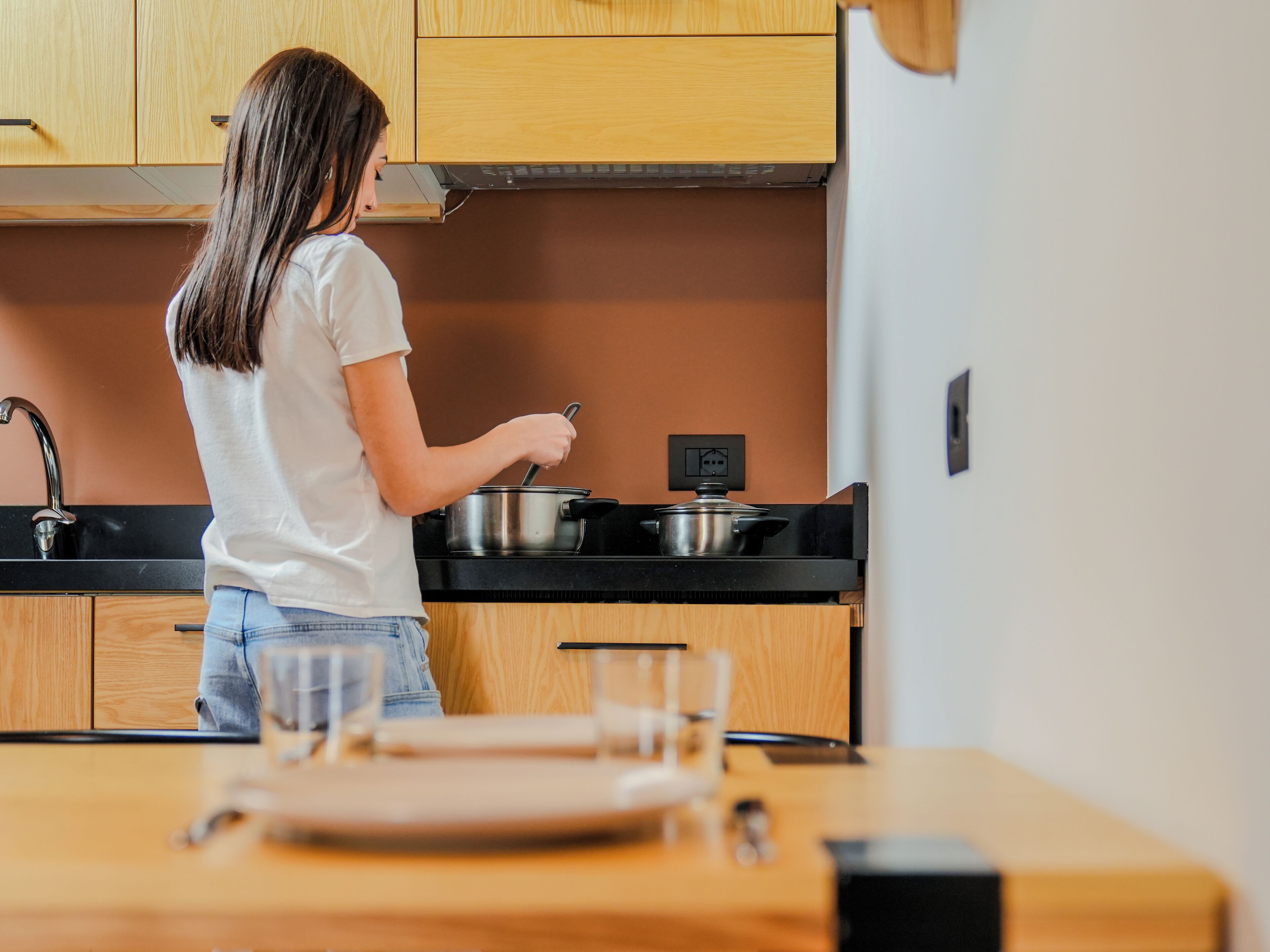 Une personne cuisine dans une cuisine moderne, dotée de meubles en bois, d’un plan de travail noir et d’une cuisinière.
