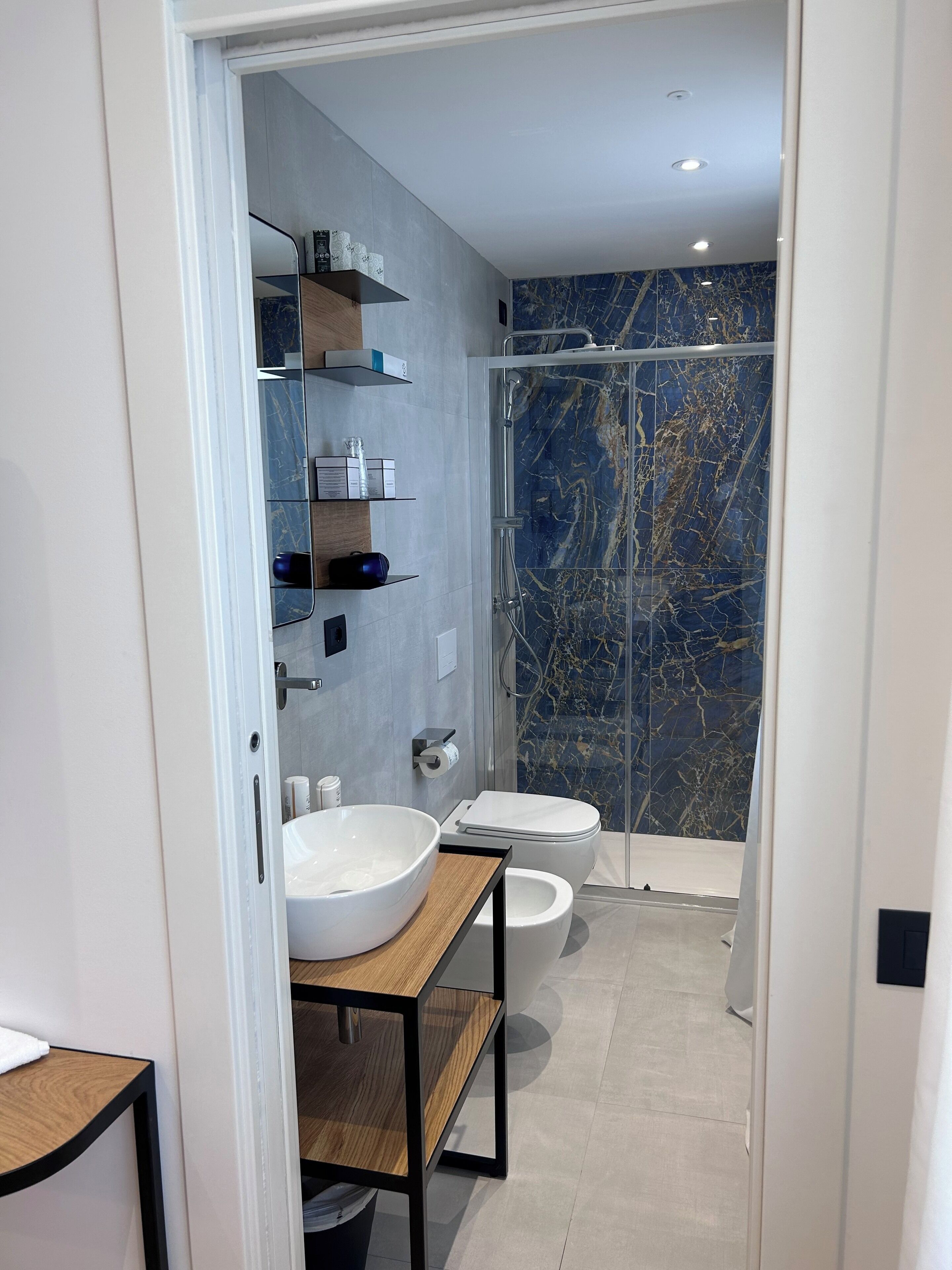 A modern bathroom with a large white sink, a glass-enclosed shower, and marble-patterned walls.