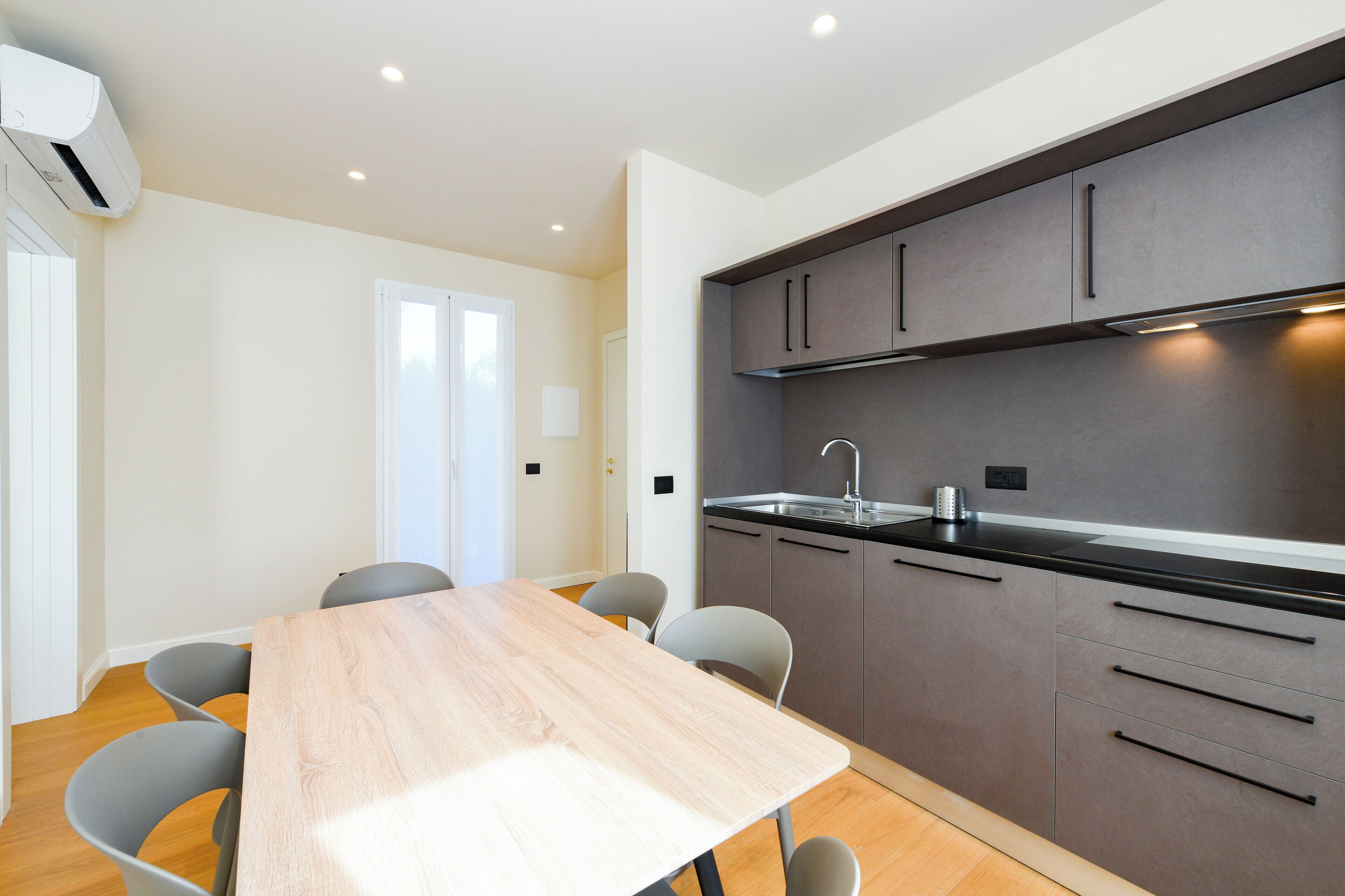 A modern kitchen with grey cabinets, a black countertop, and a wooden dining table with chairs.
