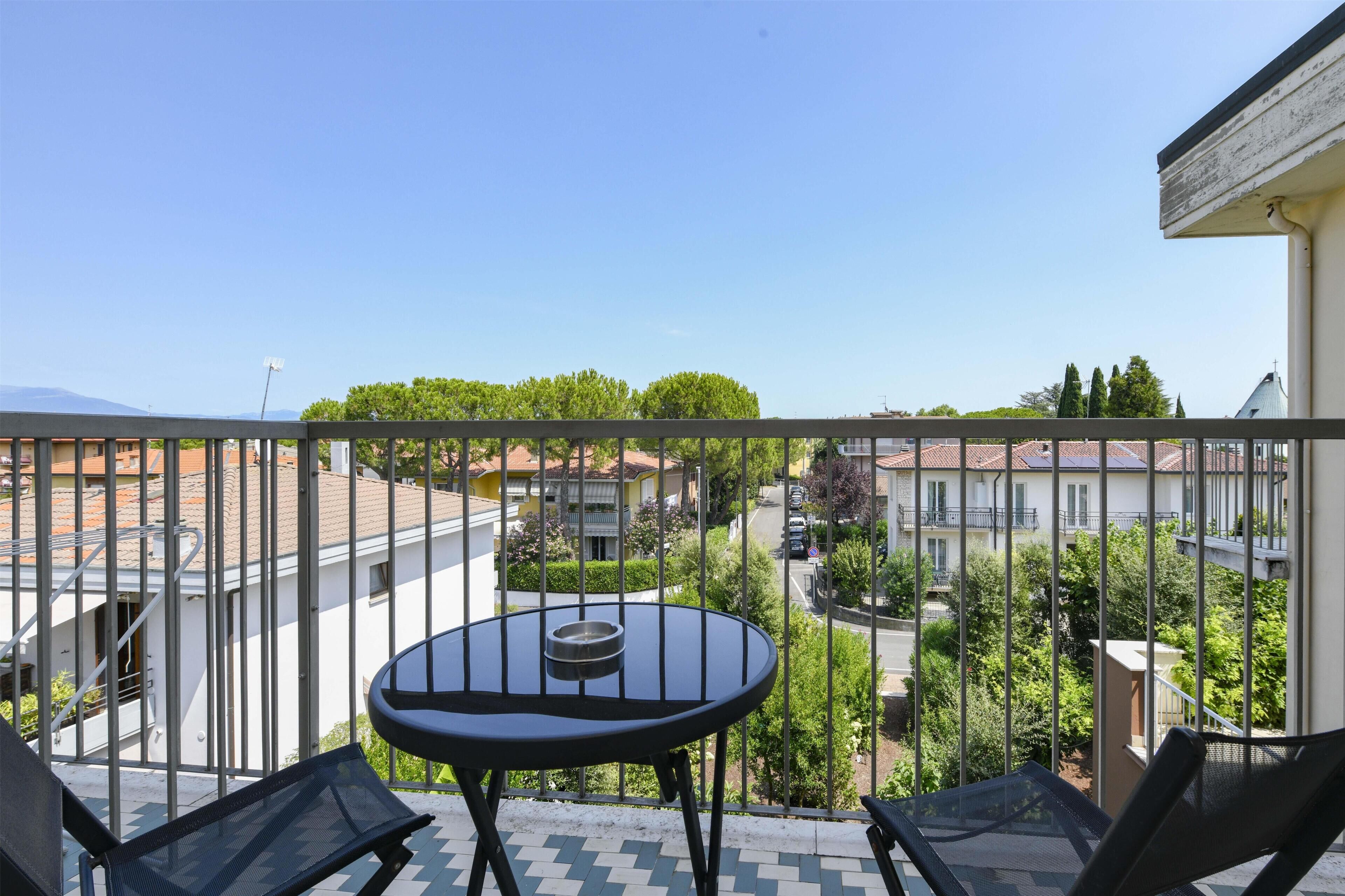 A balcony with a table and chairs, overlooking a residential area with trees and buildings.