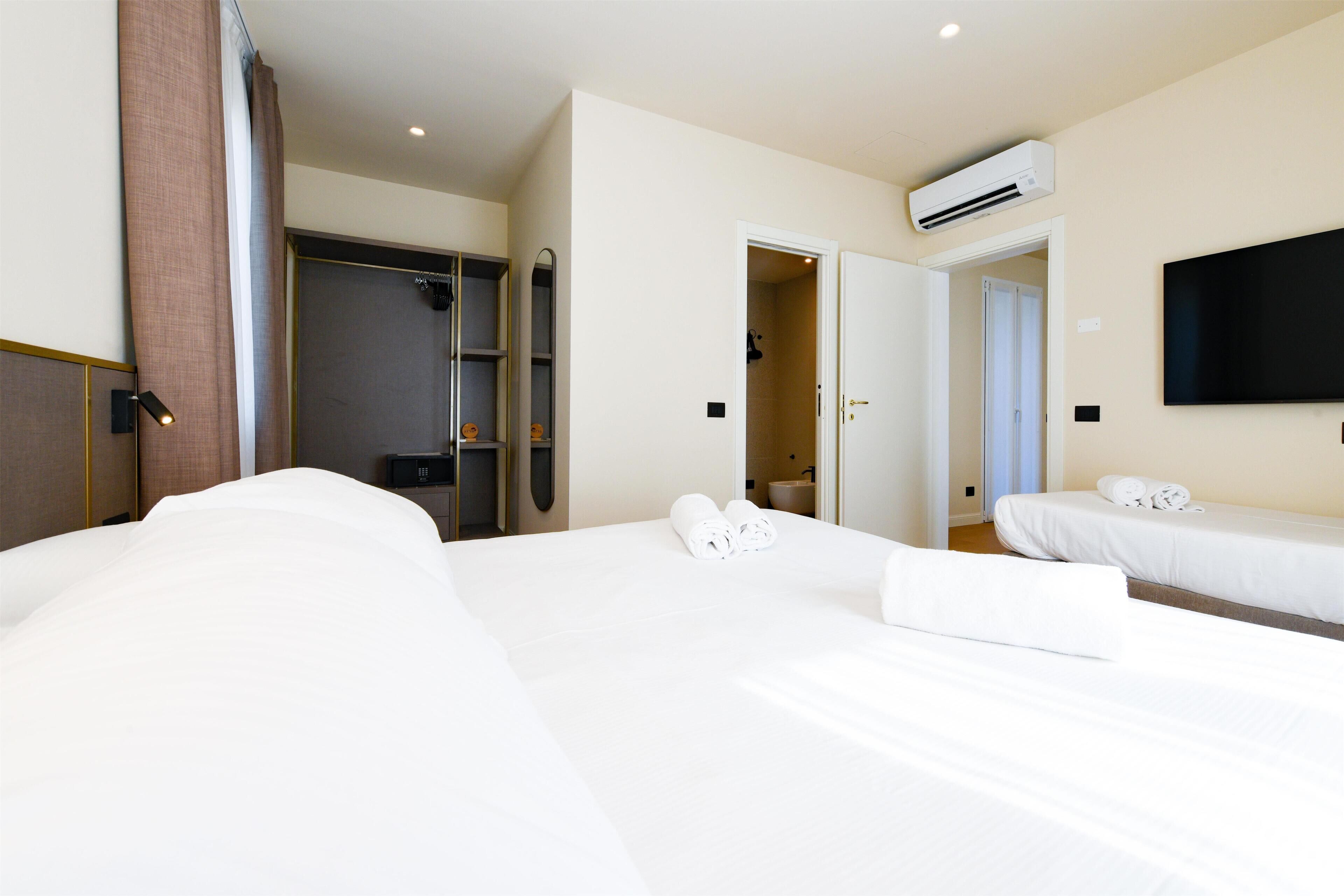 Une chambre d’hôtel avec un grand lit, un lit plus petit, une armoire, un miroir, un appareil de climatisation et un téléviseur.