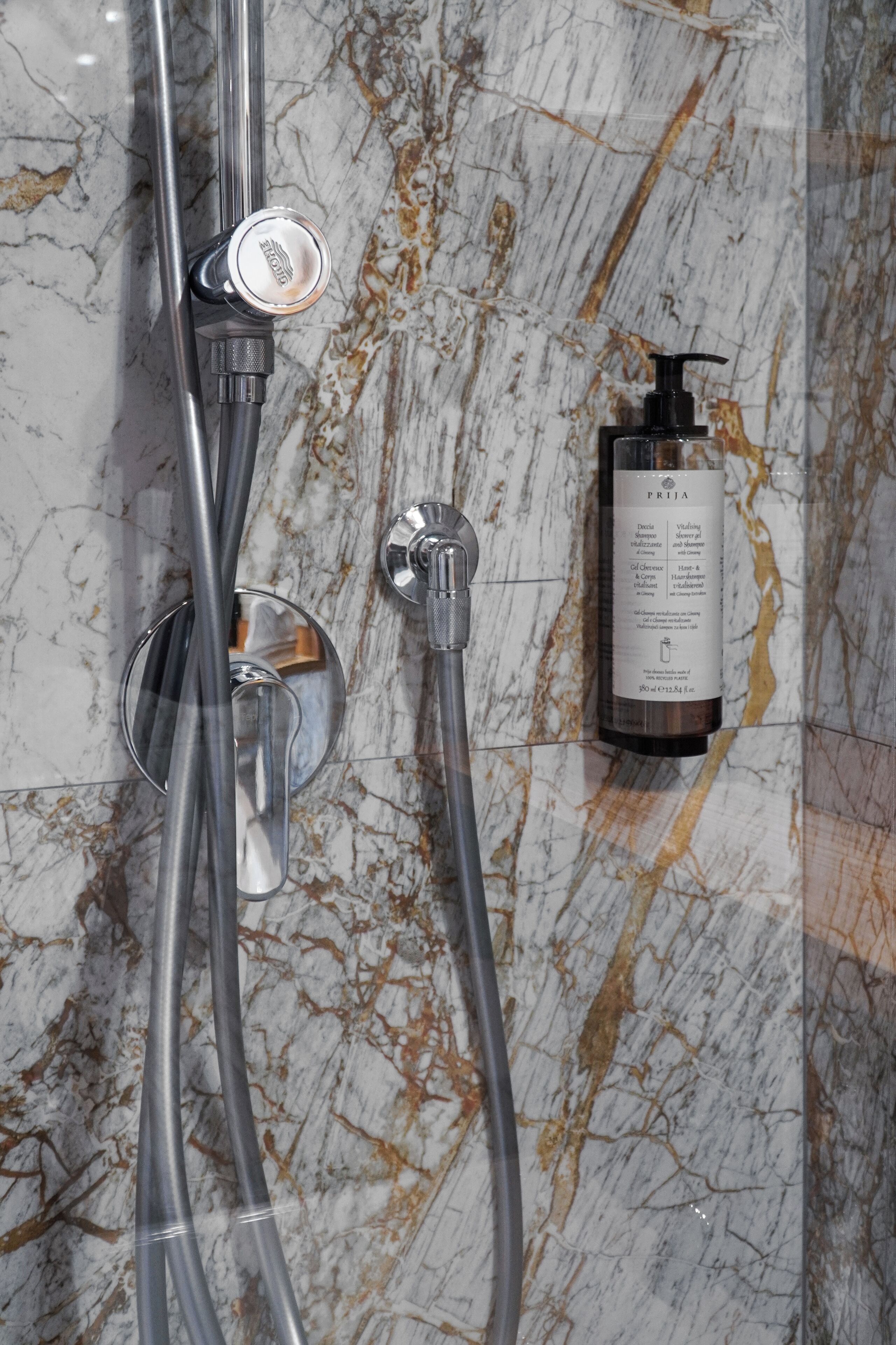 Un baño con pared de mármol, cabezal de ducha y una botella de champú.