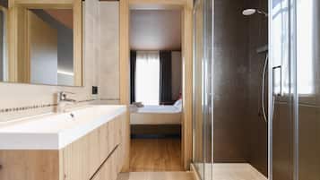 A modern bathroom with a large mirror, a shower enclosure, and a separate bedroom visible through an open door.