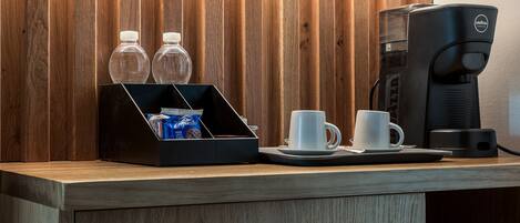 Un mostrador de recepción de madera con una cafetera, dos tazas y dos botellas de agua.