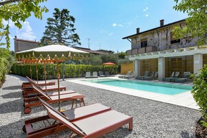 Zona piscina con sedie a sdraio e ombrelloni, piscina e un edificio con facciata rustica.