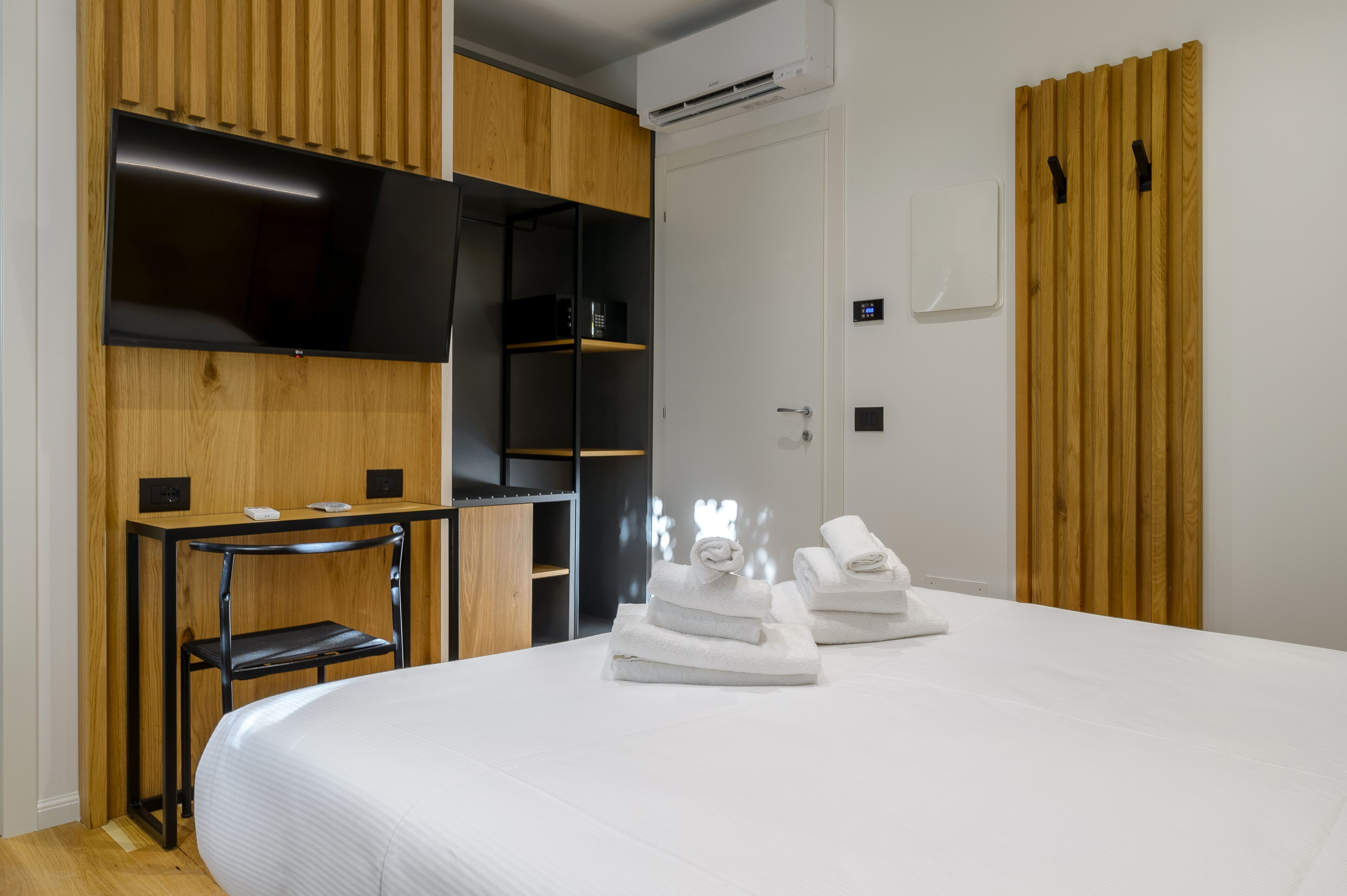 Habitación de hotel con cama, televisor montado en la pared, escritorio con silla y armario.