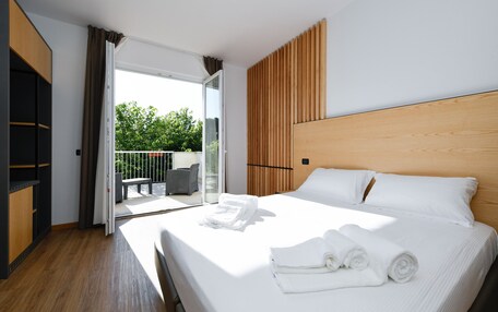 A modern hotel room with a large bed, a wooden headboard, and a balcony with outdoor furniture.