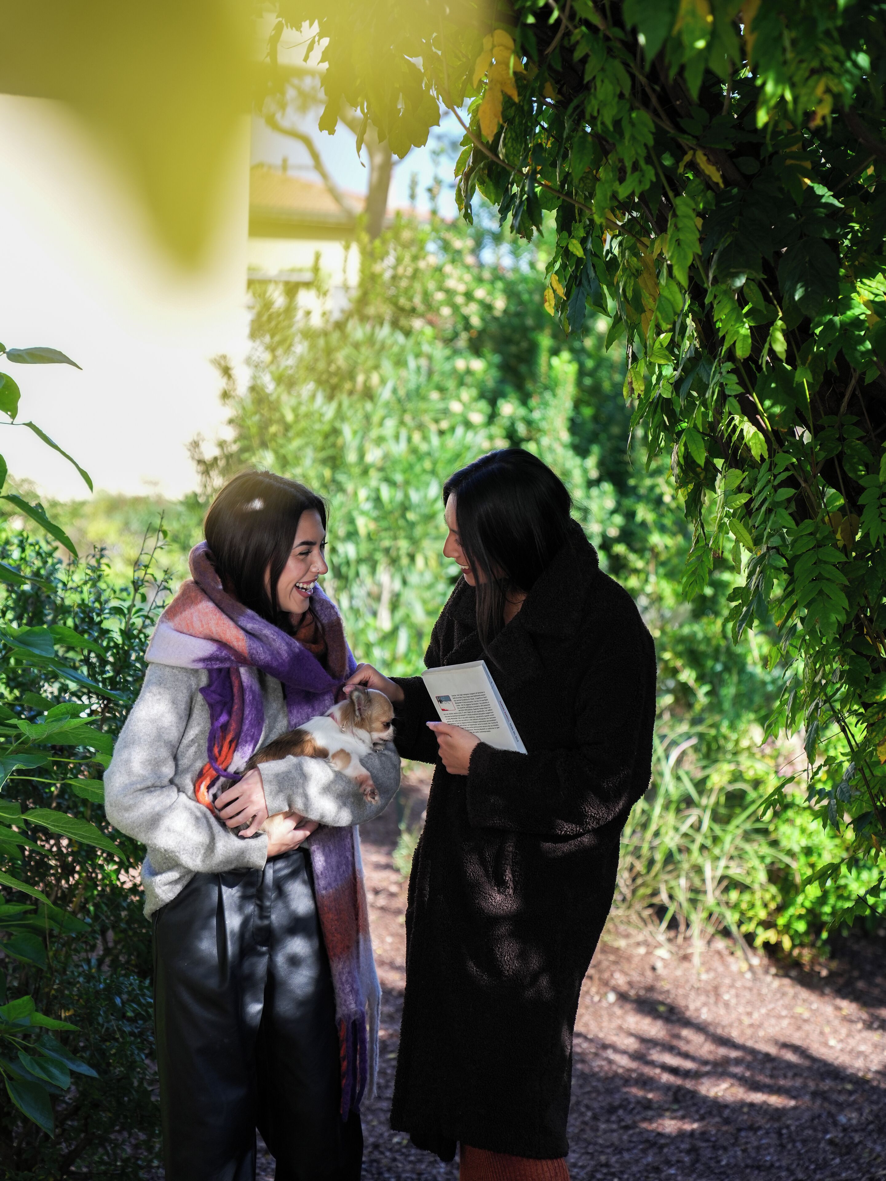 Two people in a garden-like setting, one holding a dog and the other holding a booklet.