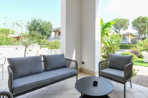 Una zona patio con un divano e una poltrona grigi, un tavolo rotondo e vista su un quartiere residenziale.