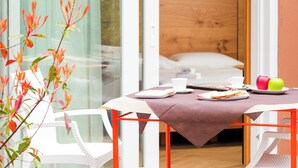 Uma sala de jantar com mesa posta para dois, uma cama ao fundo e vista para o exterior.