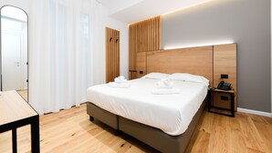 Quarto moderno com uma cama grande, cabeceira de madeira, mesas de cabeceira e um espelho.