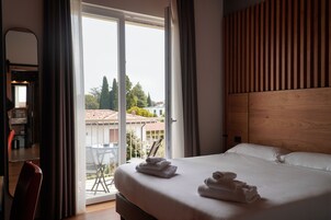 Camera d'albergo con un letto grande, una testiera in legno e vista all'esterno tramite una porta scorrevole in vetro.