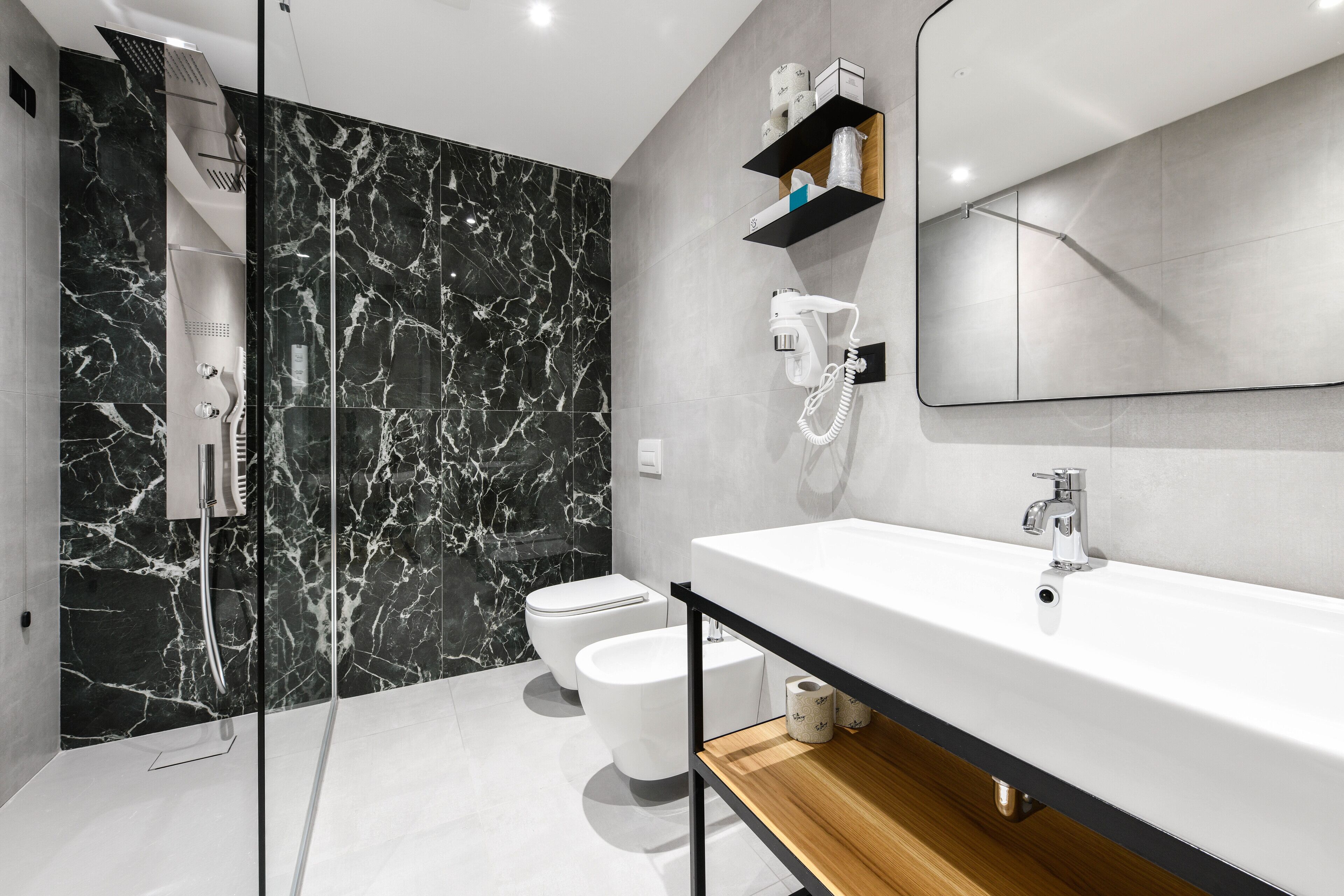 Une salle de bain moderne avec un lavabo blanc, un pare-chocs en marbre noir et une douche à l’italienne en verre.