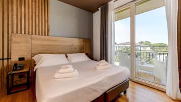 Camera d'albergo con un letto grande, una testiera in legno, un comodino con un telefono e un balcone con vista.