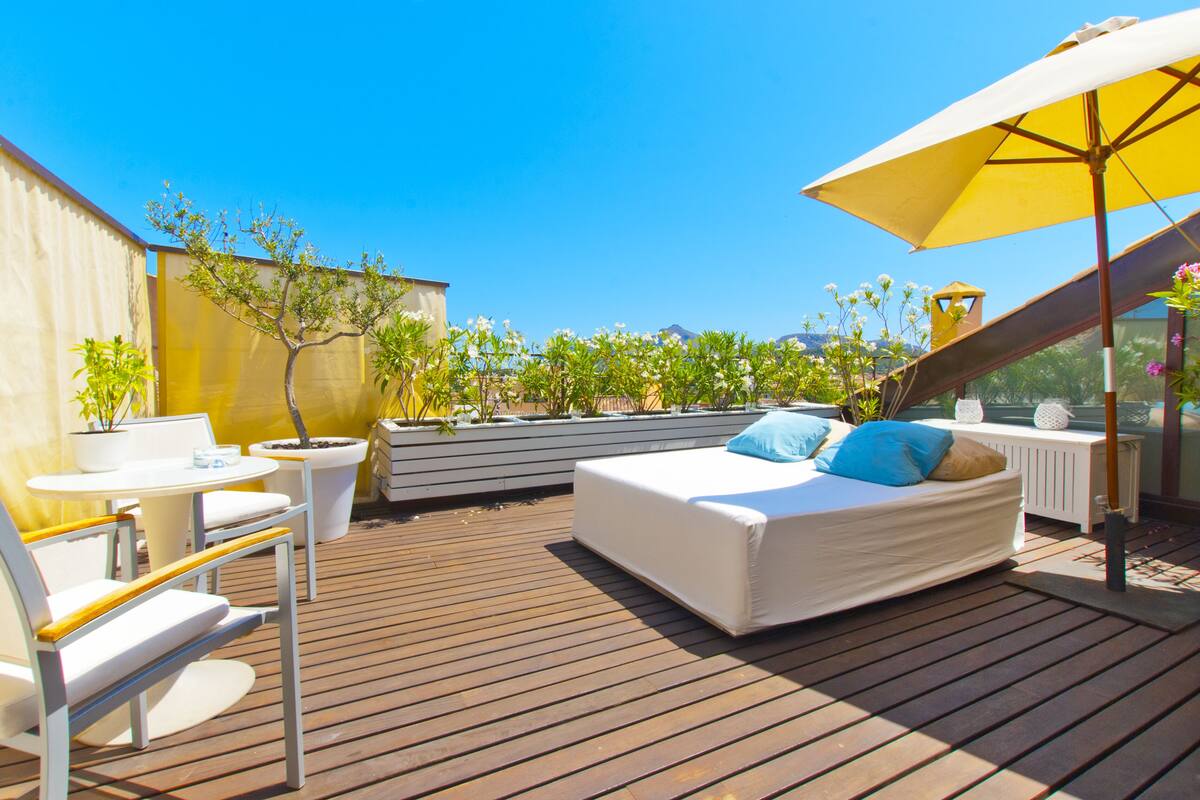Une terrasse sur le toit aménagée avec un lit, un coin salon et des plantes en pot.