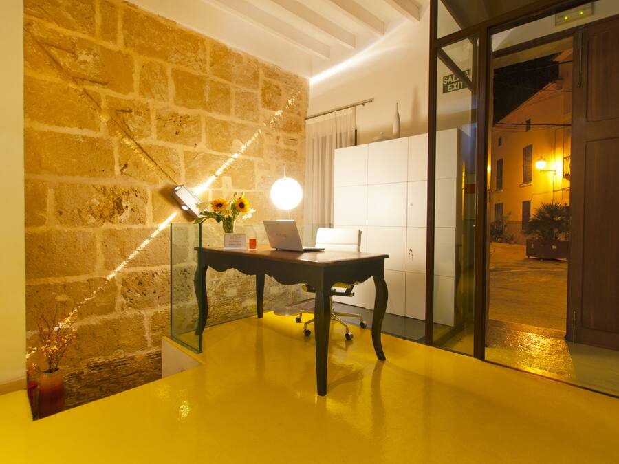 Una habitación con pared de piedra, un escritorio con una computadora portátil, un jarrón con flores y una puerta de vidrio que da al exterior.