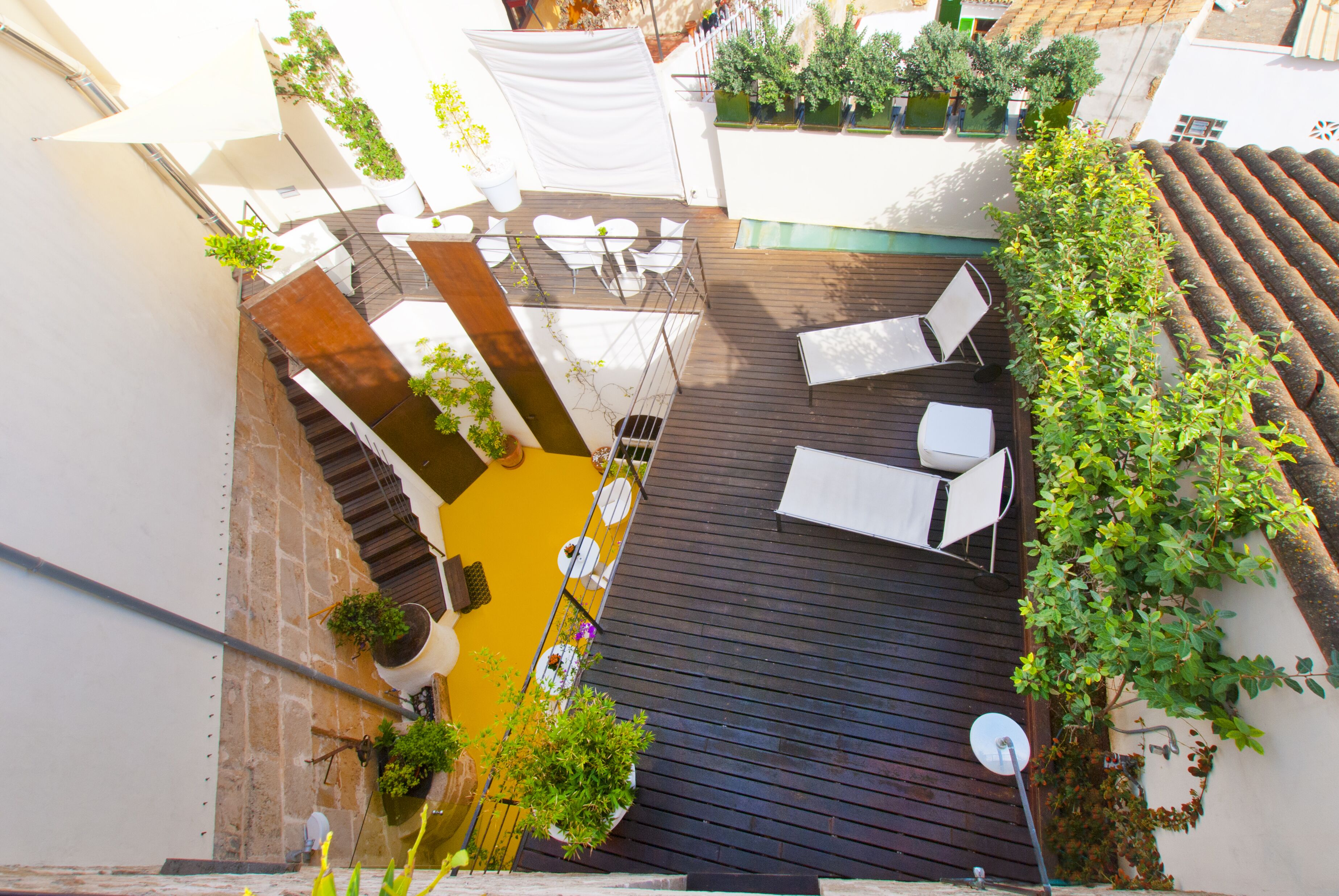 Terraza en la azotea con piso de madera, muebles de exterior blancos y plantas en macetas.